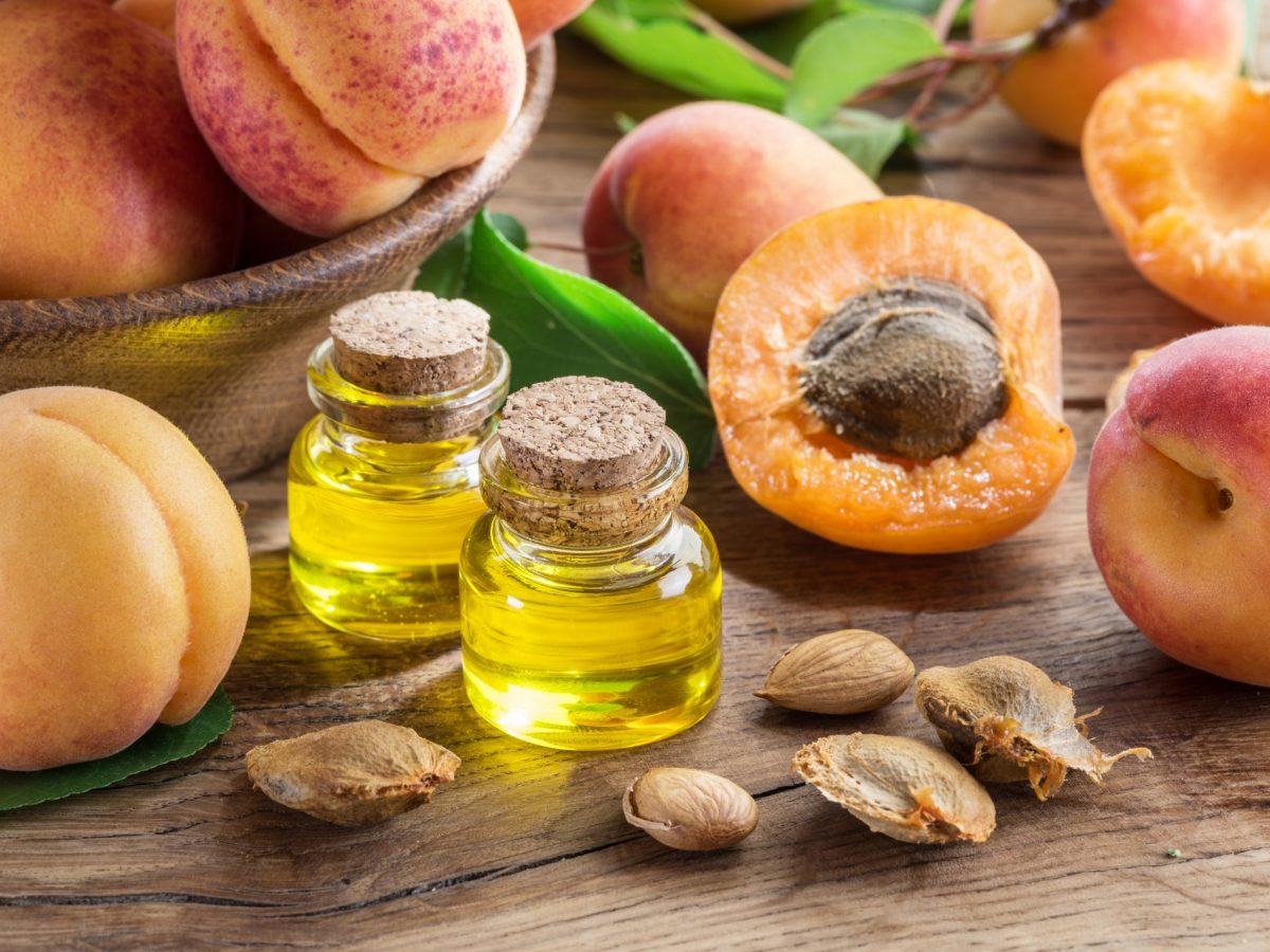 Deux flacons d'huile de noyau d'abricot avec des abricots coupés et des noyaux, posés sur une table