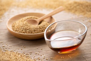 Récipient avec de l'huile de sésame avec en arrière plan un bol de graines de sésame avec une cuillère