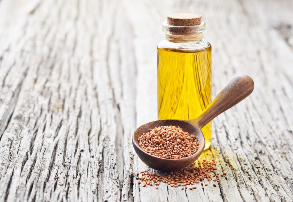 Cuillère en bois contenant des graines de caméline avec une fiole d'huile de caméline en arrière plan