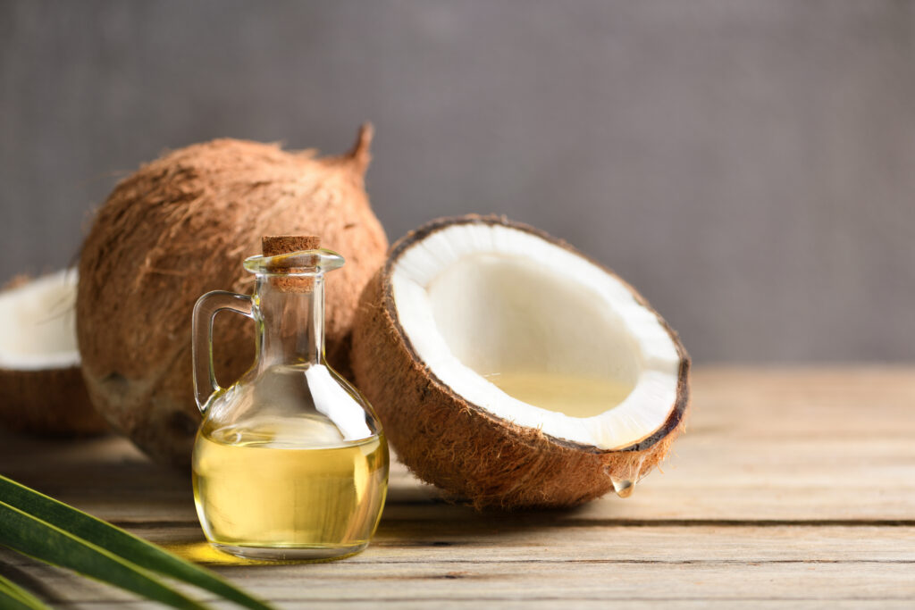 gros plan sur une fiole d'huile de coco ainsi qu'une coco entière et une coupée en deux en arrière plan