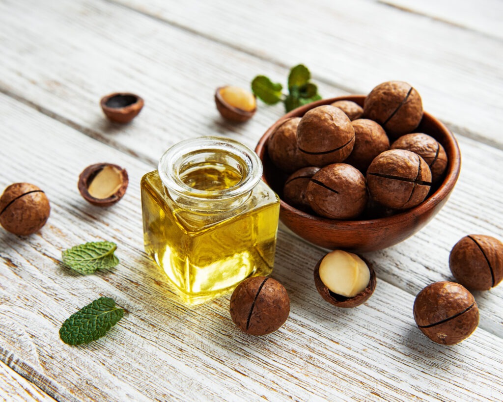 gros plan sur un flacon d'huile de macadamia avec un petit bol et des noix de macadamia dedans et autour, posés sur une table