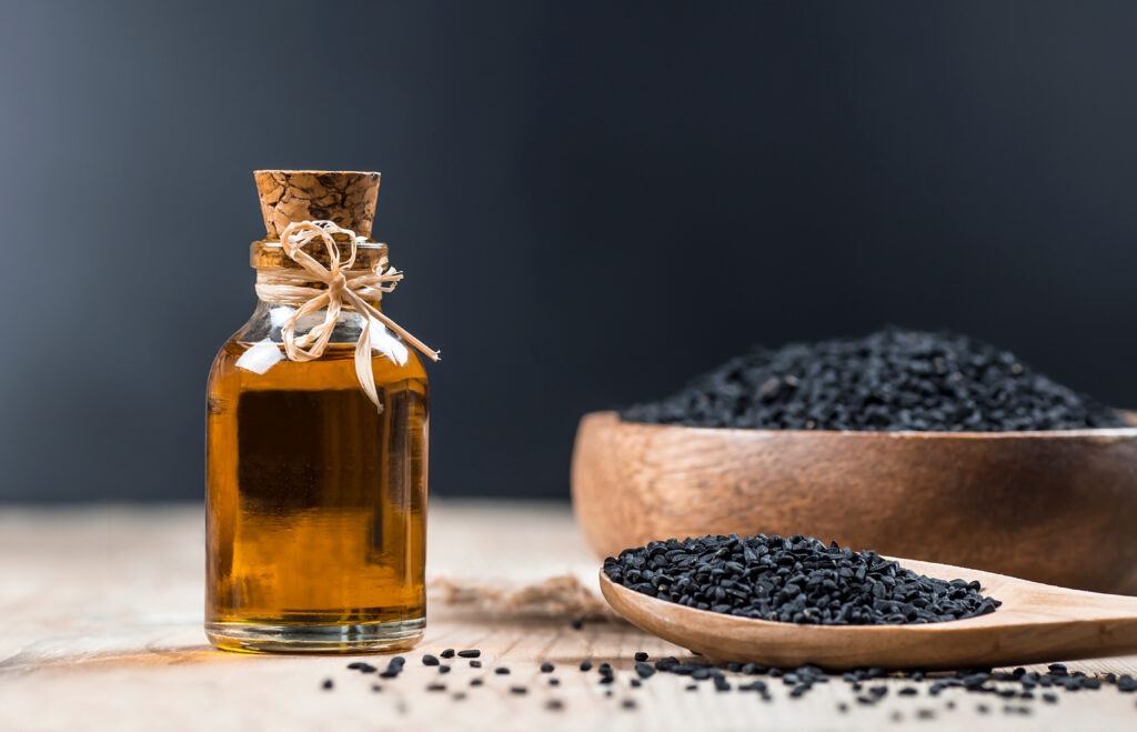 Fiole d'huile de nigelle avec une cuillère de graines de nigelle et un bol de graines de nigelle en arrière plan