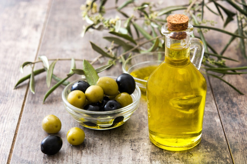 Flacon d'huile d'olive et de bol d'olives avec une branche posés sur une table