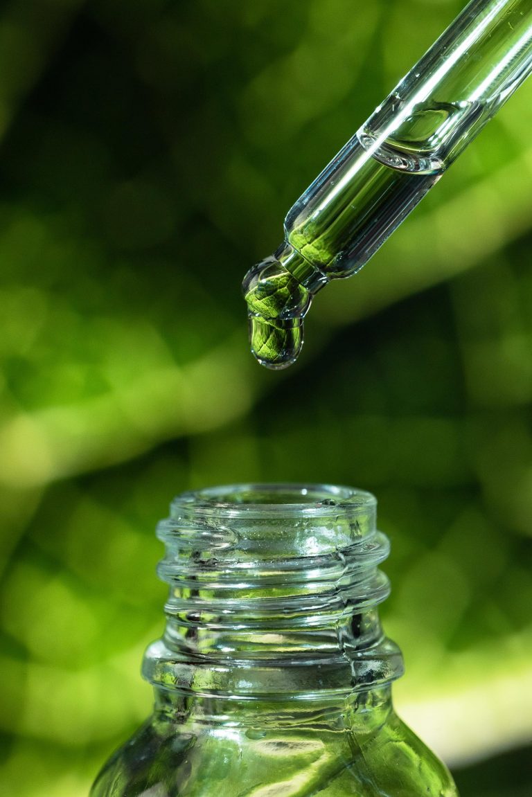 Drop of oil on a background of green leaves. Cosmetic pipette with essence.